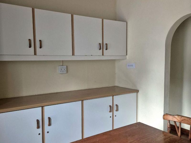 A dated kitchen area featuring white built-in cabinetry, laminate countertops, and a distinctive timber-paneled ceiling with an arched entryway.