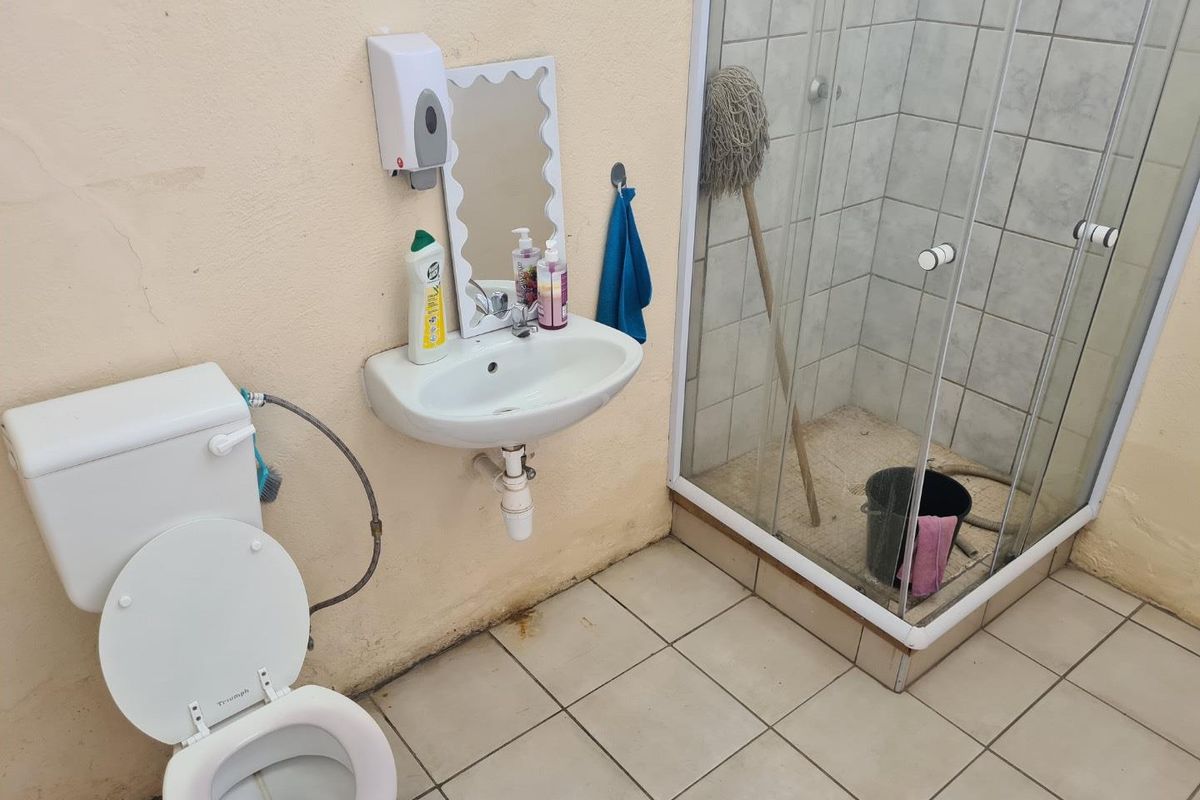 A functional bathroom featuring a wall-mounted basin, toilet, and a glass-enclosed shower with tiled flooring.