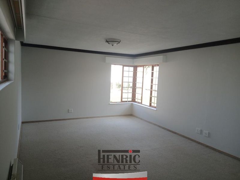 A spacious, empty living room featuring a bay window, neutral carpeting, and crown molding, providing a blank canvas for interior design.