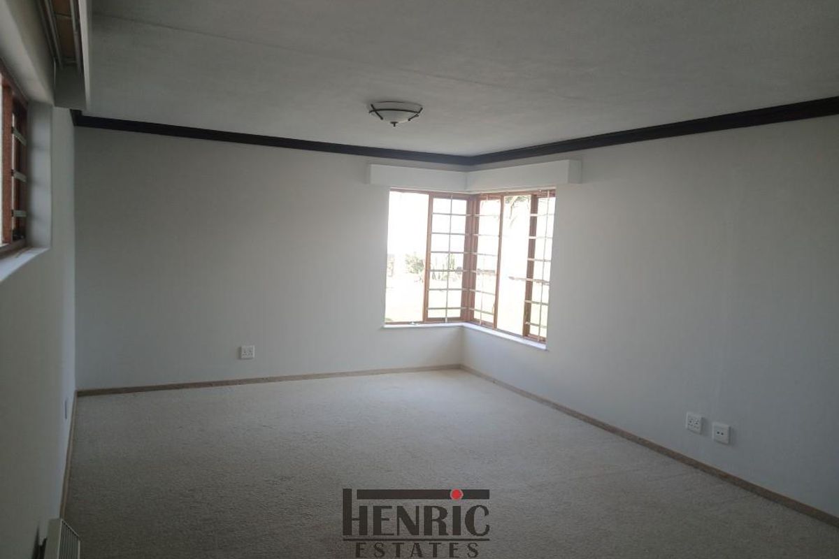 A spacious, empty living room featuring a bay window, neutral carpeting, and crown molding, providing a blank canvas for interior design.