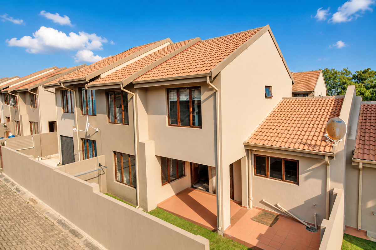 Rear view of a multi-story townhouse featuring a tiled patio, terracotta roof tiles, and a private enclosed garden area.