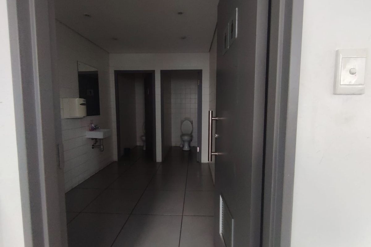 A functional commercial bathroom facility featuring tiled flooring, wall-mounted sinks, and individual toilet cubicles.