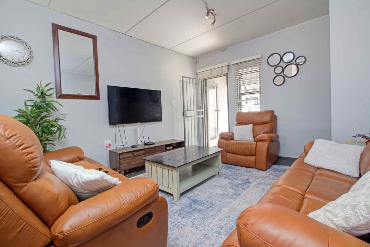 A comfortable living room featuring tiled flooring, a security gate leading to the exterior, and neutral wall finishes.