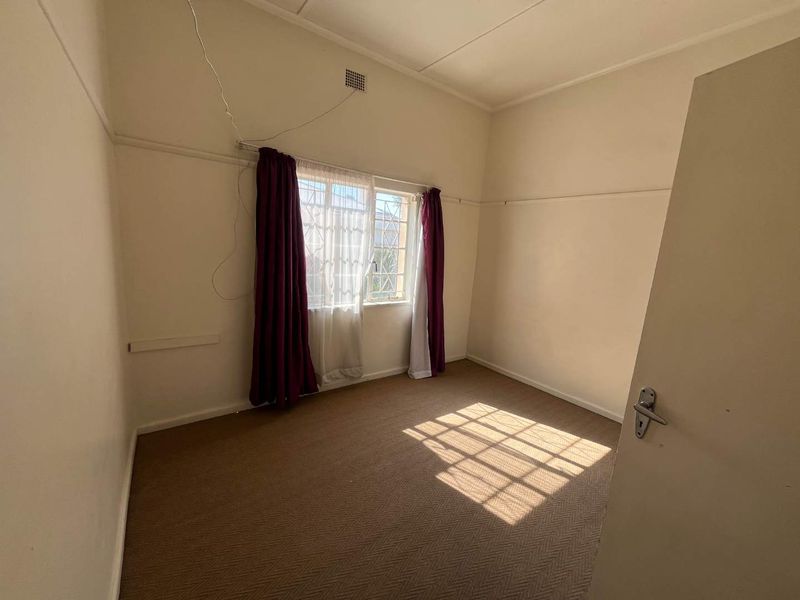 An empty bedroom featuring carpet flooring, a window with security bars, and a picture rail, requiring minor cosmetic updates.