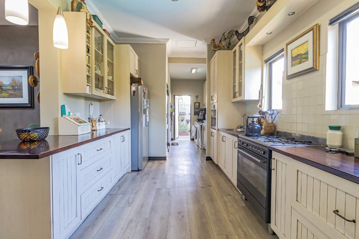 A functional galley-style kitchen featuring cream cabinetry, dark wood countertops, a gas stove, and light-toned laminate flooring with a direct view to the laundry area.