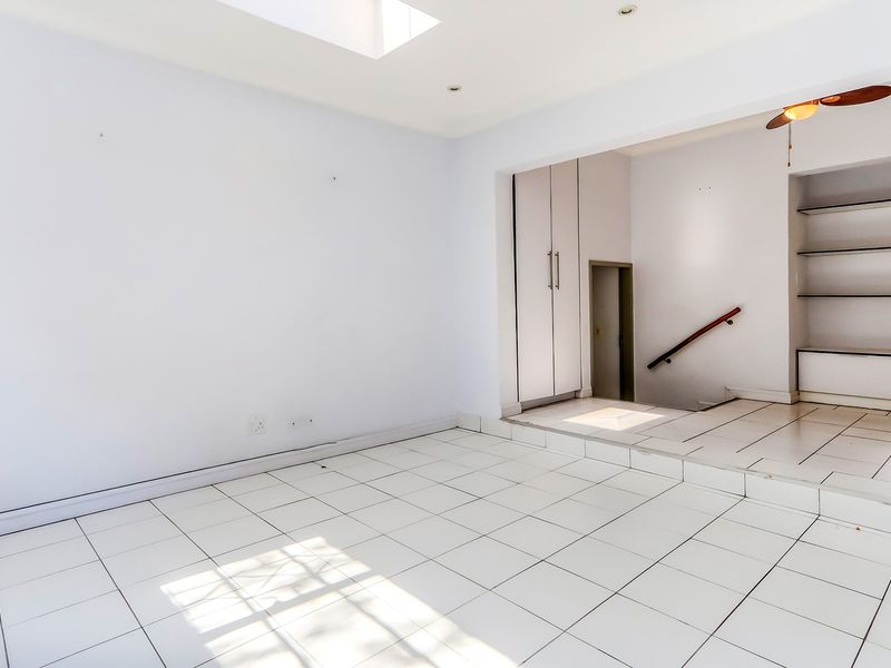 An empty, open-plan living area featuring white tiled flooring, a skylight, built-in storage cabinetry, and a staircase with a handrail.
