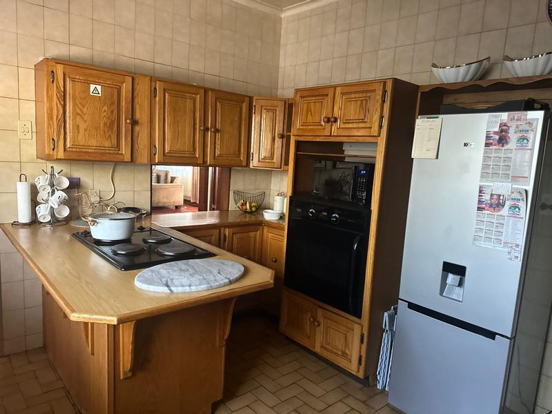 A dated kitchen featuring wooden cabinetry, a built-in oven, an electric hob, and tiled wall finishes, offering potential for a modern renovation.
