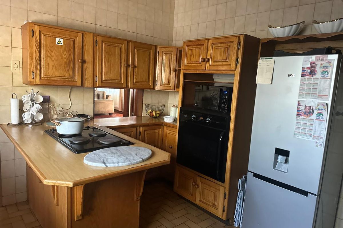 A dated kitchen featuring wooden cabinetry, a built-in oven, an electric hob, and tiled wall finishes, offering potential for a modern renovation.