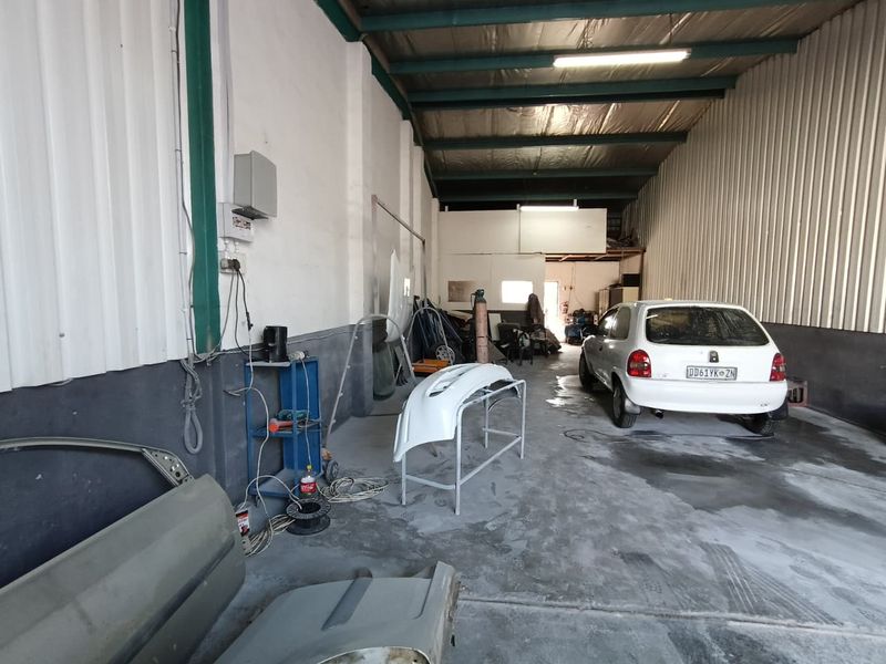 Industrial workshop space featuring exposed steel roof trusses, corrugated metal wall cladding, and concrete flooring, currently utilized for automotive repair and maintenance.