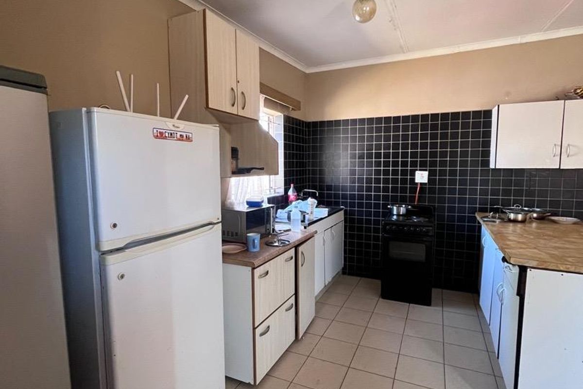 Functional kitchen featuring tiled flooring, dark tiled splashbacks, laminate countertops, and built-in cabinetry with a freestanding stove.