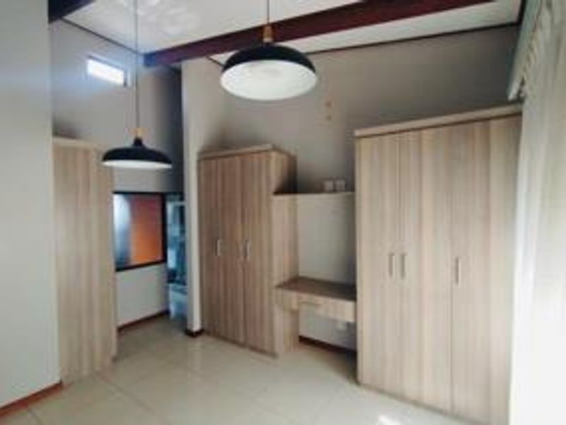 A bedroom featuring extensive built-in cabinetry, a integrated desk, tiled flooring, and exposed ceiling beams with modern pendant lighting.