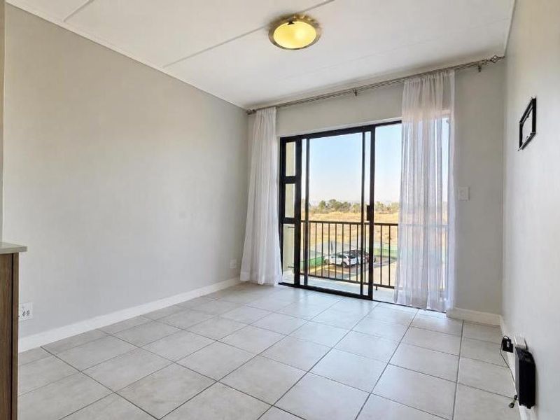 An open-plan living area featuring tiled flooring, a ceiling light fixture, and a sliding glass door leading to a balcony.