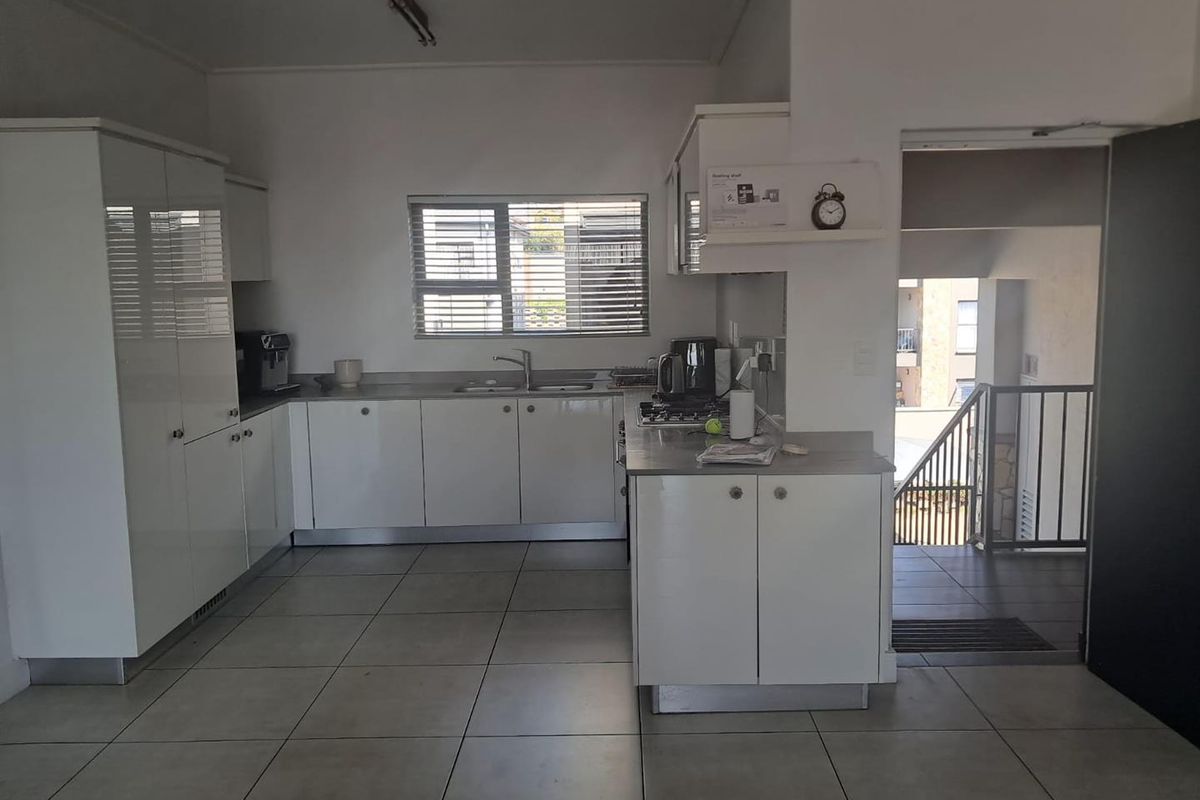 A functional kitchen featuring white high-gloss cabinetry, tiled flooring, and a built-in hob, with an adjacent staircase leading to the apartment entrance.
