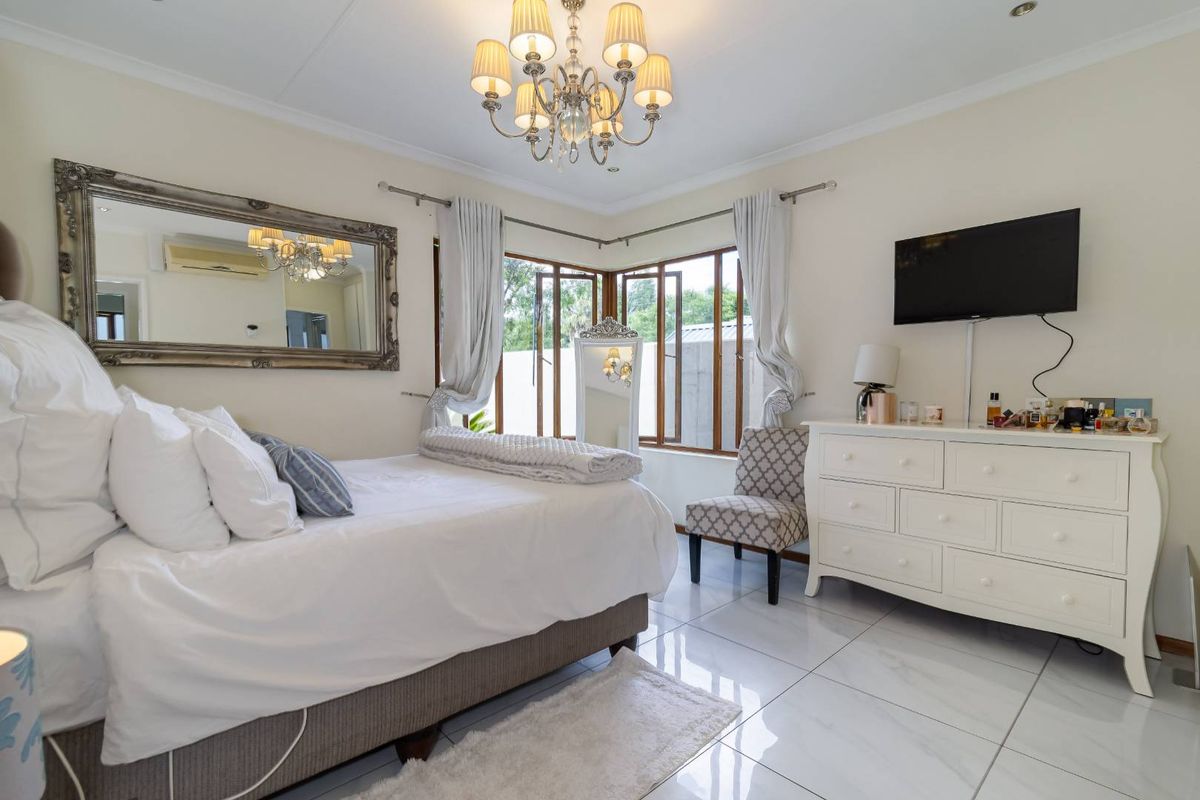 A well-maintained bedroom featuring large corner windows, polished tile flooring, and a decorative chandelier, offering a bright and comfortable living space.