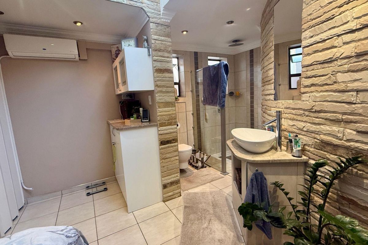 A functional bathroom featuring a vessel sink vanity, glass-enclosed shower, and stone-clad feature walls, complemented by tiled flooring and integrated lighting.