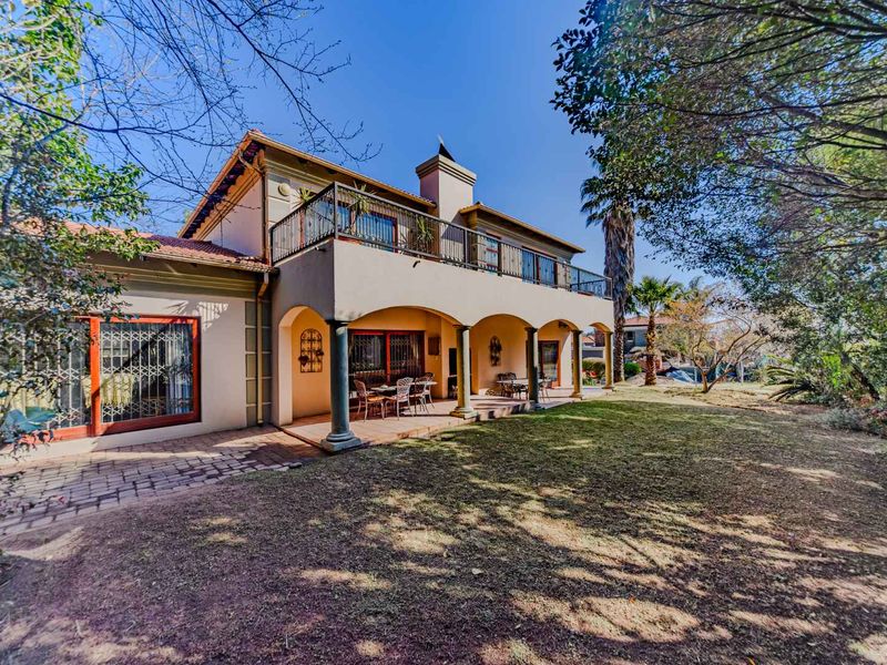 Rear view of the double-story house featuring a spacious covered patio, an upper-level balcony, and a well-established garden area.