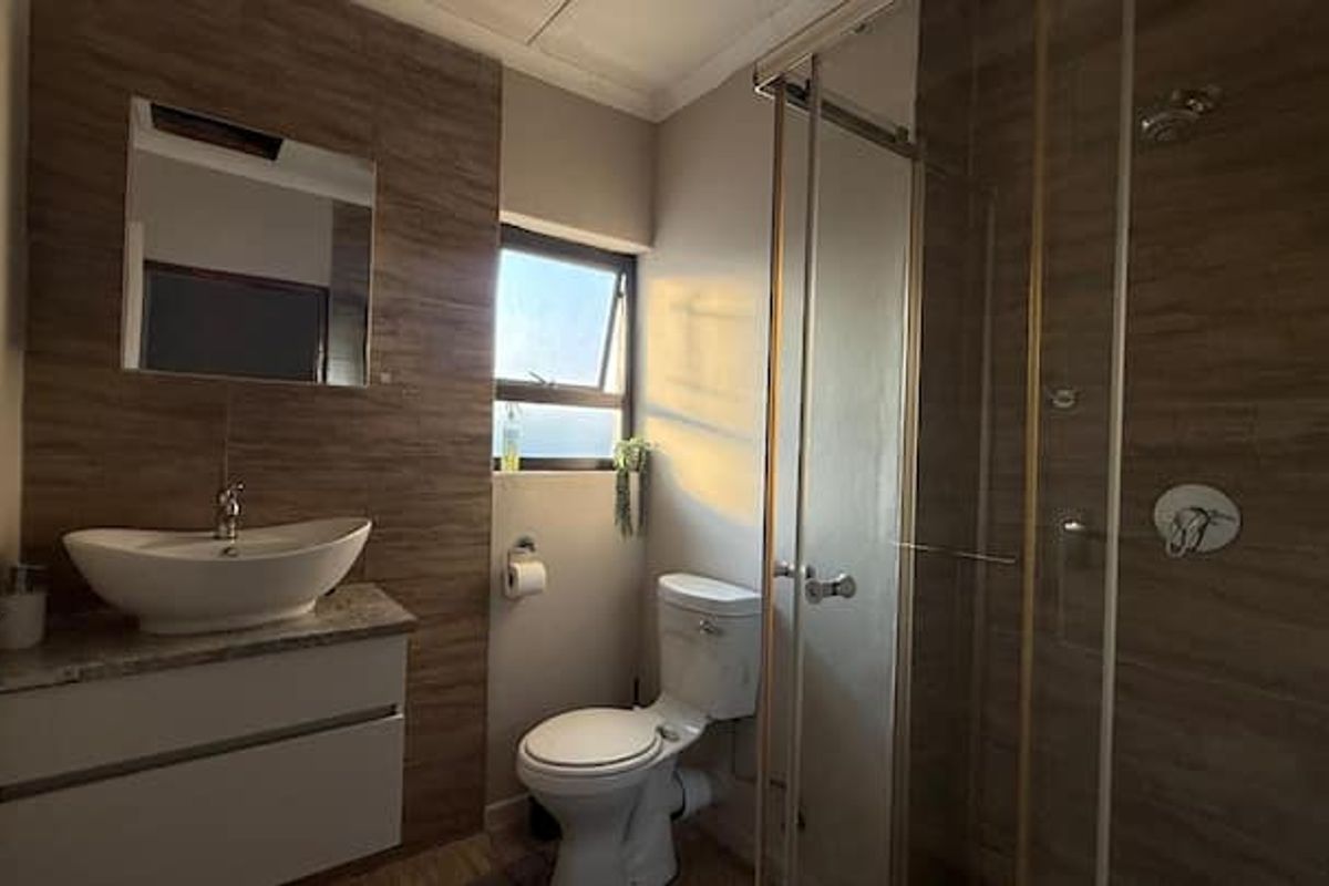 Modern bathroom featuring a vessel sink on a stone-topped vanity, a glass-enclosed shower, and stylish wood-look tiled feature wall.