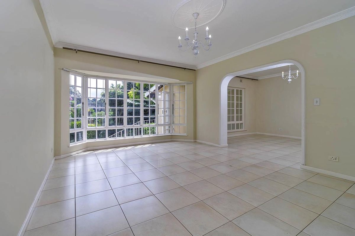 Spacious living area featuring large bay windows, tiled flooring, decorative ceiling rose, and an arched entryway leading to an adjacent room.