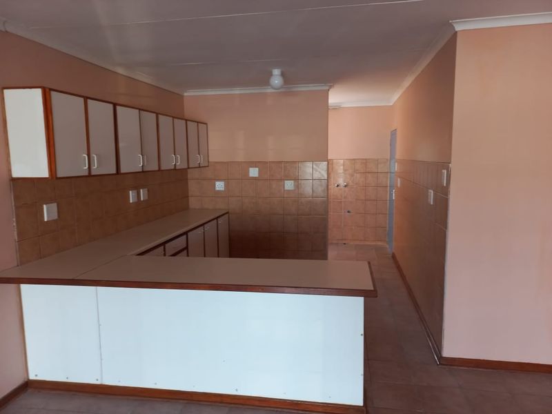 An empty, dated kitchen featuring built-in cabinetry, laminate countertops, and tiled splashbacks, offering a blank canvas for modern renovation.