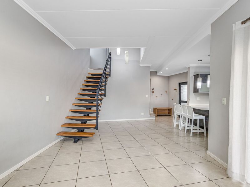 Spacious open-plan living area featuring a modern floating staircase, neutral tiled flooring, and a functional kitchen with a breakfast island.