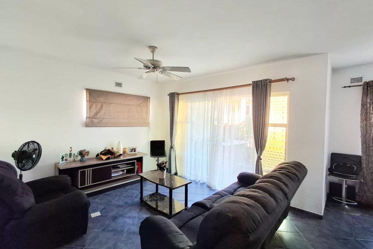 A living room featuring tiled flooring, a ceiling fan, and a large sliding glass door providing natural light.