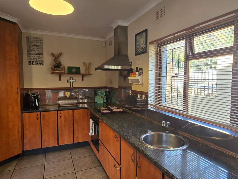 Functional kitchen featuring wood-finish cabinetry, granite countertops, stainless steel sink, and integrated extractor fan with natural light from large windows.
