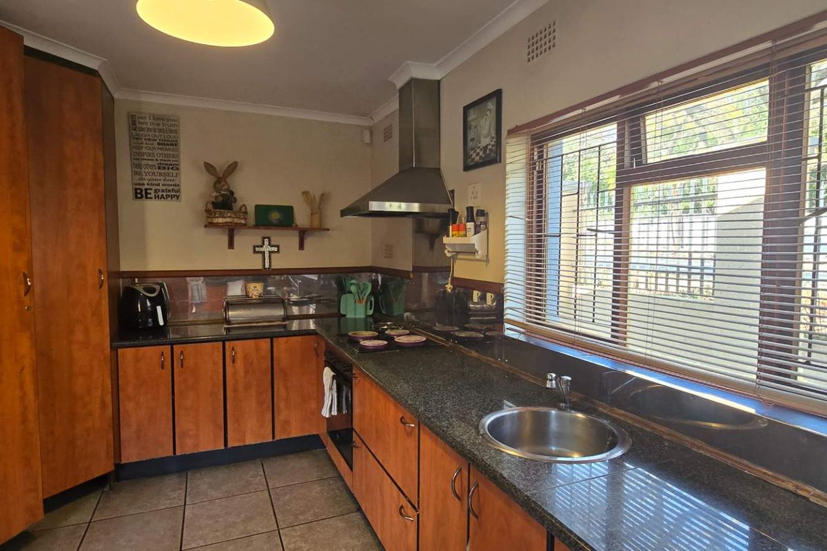 Functional kitchen featuring wood-finish cabinetry, granite countertops, stainless steel sink, and integrated extractor fan with natural light from large windows.