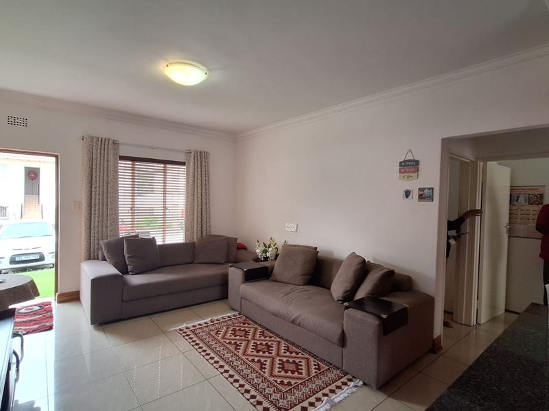 A living room featuring tiled flooring, ceiling cornice, and natural light through an aluminium window, with direct access to the exterior via a security gate.