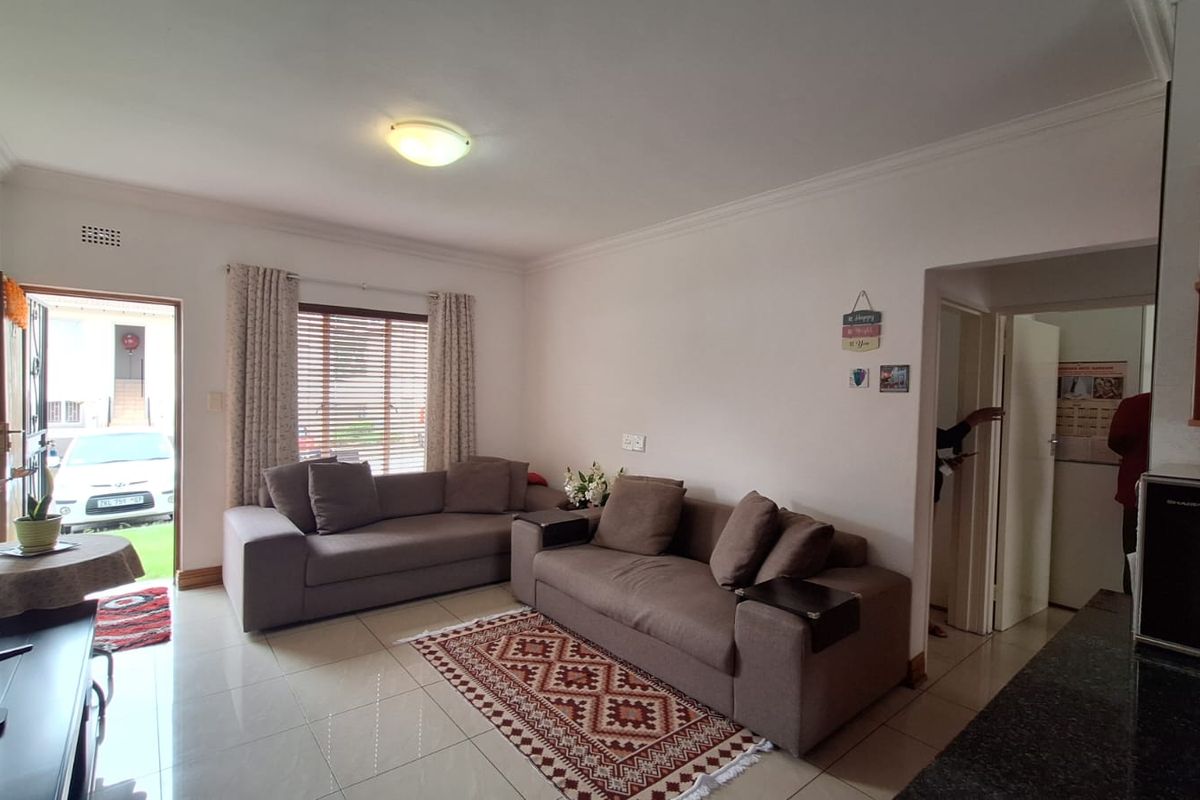 A living room featuring tiled flooring, ceiling cornice, and natural light through an aluminium window, with direct access to the exterior via a security gate.