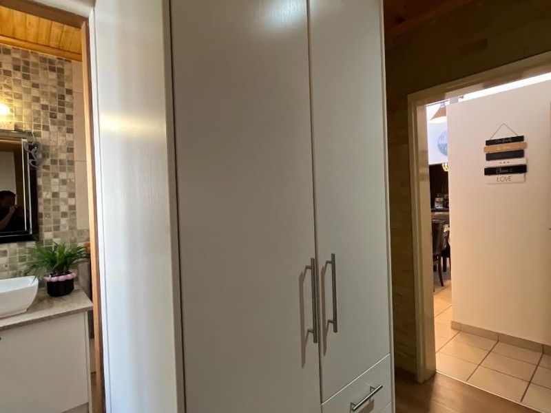 A hallway featuring a large built-in cupboard with modern hardware, laminate flooring, and a timber-clad ceiling, providing access to an adjacent bathroom.