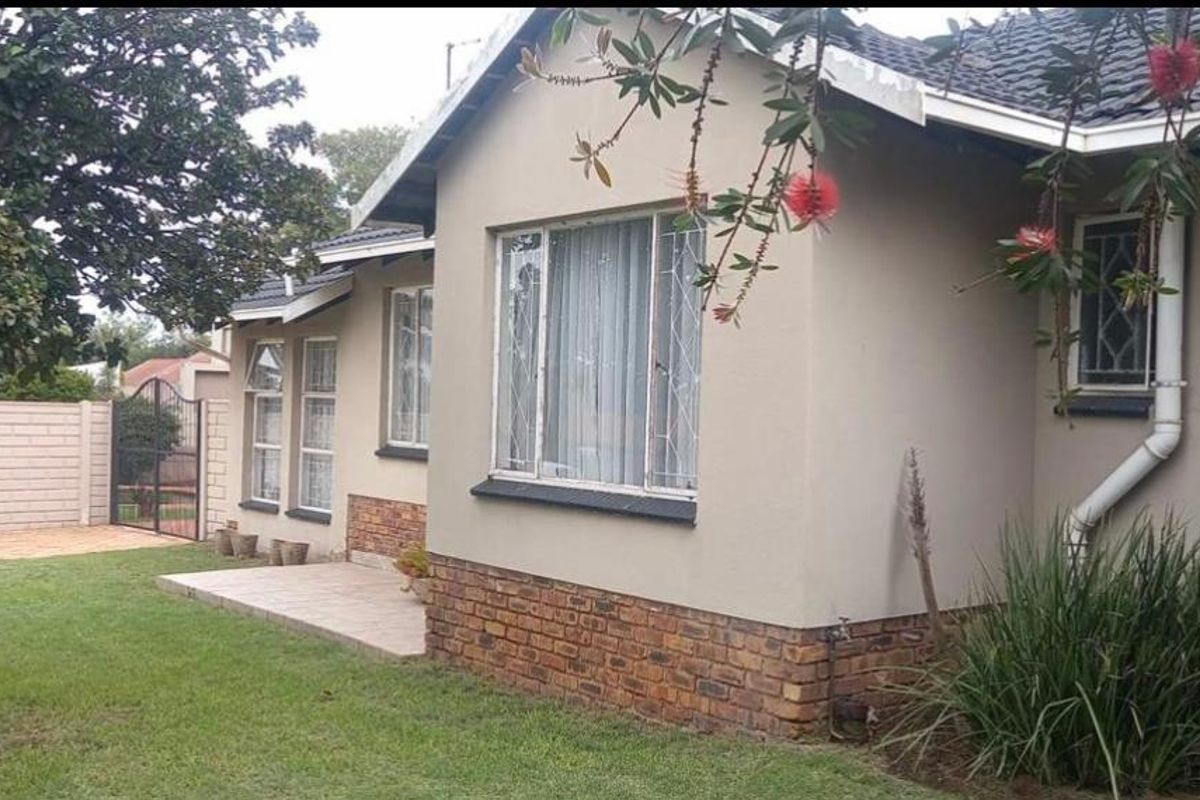 A view of the rear exterior of the house, featuring a tiled patio area, brick base detailing, and established garden surroundings.