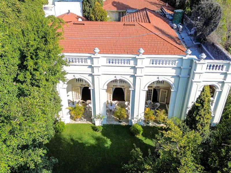 Aerial view of a classic guest house featuring a terracotta tiled roof, an elegant arched patio, and a well-maintained garden.