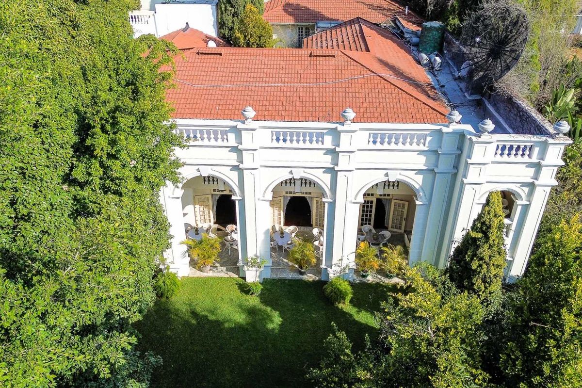 Aerial view of a classic guest house featuring a terracotta tiled roof, an elegant arched patio, and a well-maintained garden.