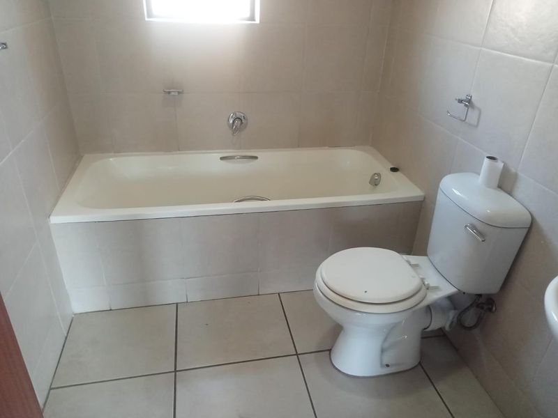 A functional bathroom featuring a built-in bathtub, toilet, and neutral ceramic tiling throughout.