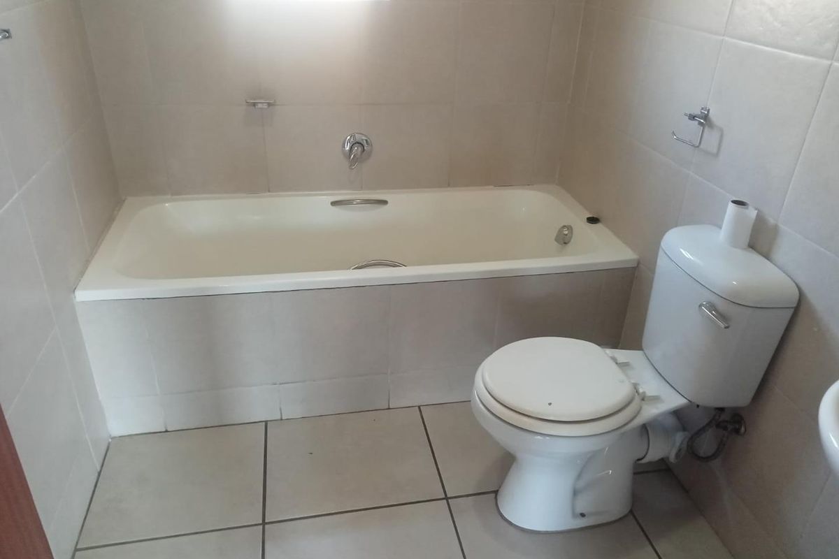 A functional bathroom featuring a built-in bathtub, toilet, and neutral ceramic tiling throughout.