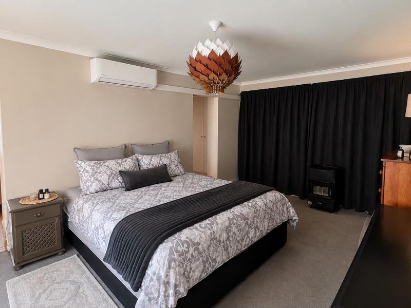 A spacious bedroom featuring neutral wall tones, carpeted flooring, a split-system air conditioner, and built-in storage cupboards.