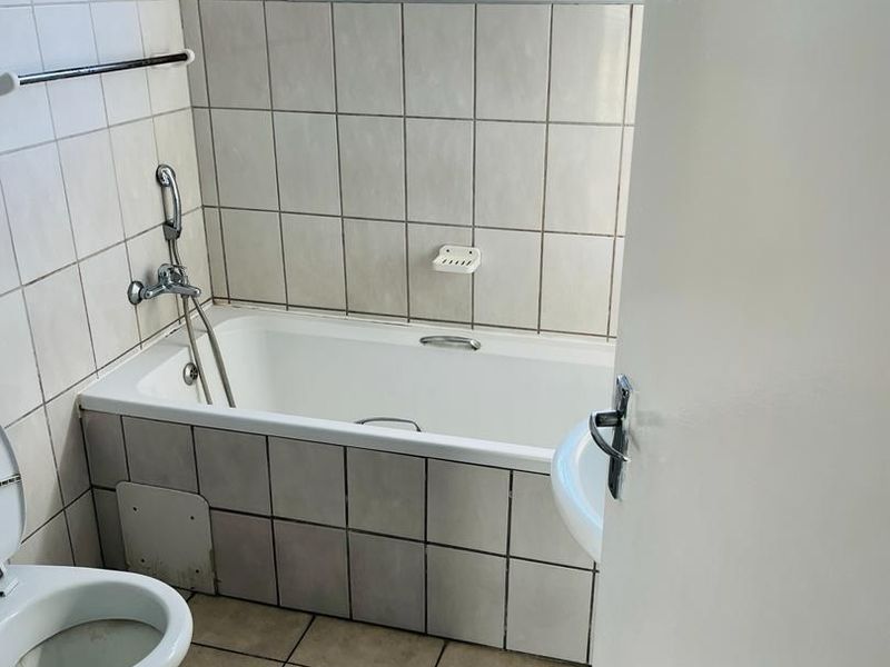 A functional bathroom featuring a bathtub with a handheld shower mixer, tiled walls and floors, and a top-hung window for natural ventilation.