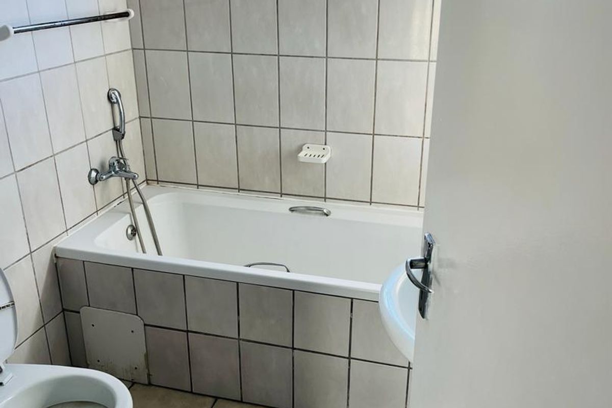 A functional bathroom featuring a bathtub with a handheld shower mixer, tiled walls and floors, and a top-hung window for natural ventilation.