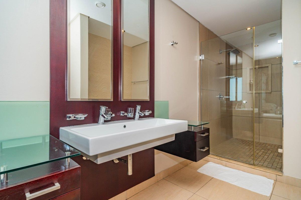 Modern bathroom featuring a double vanity with wall-mounted basins, dark wood cabinetry, and a spacious walk-in glass shower enclosure with tiled finishes.