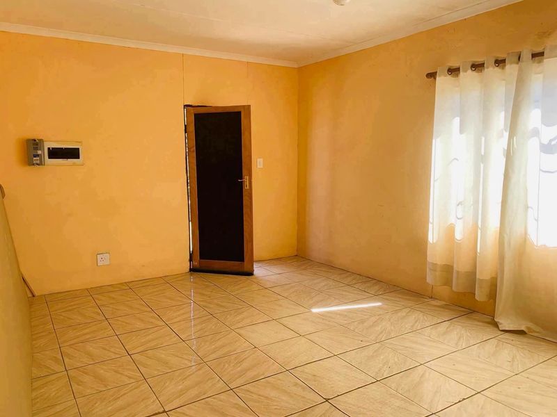 An empty living room featuring tiled flooring, a wall-mounted electrical distribution board, and a curtain rod, ready for personalization.