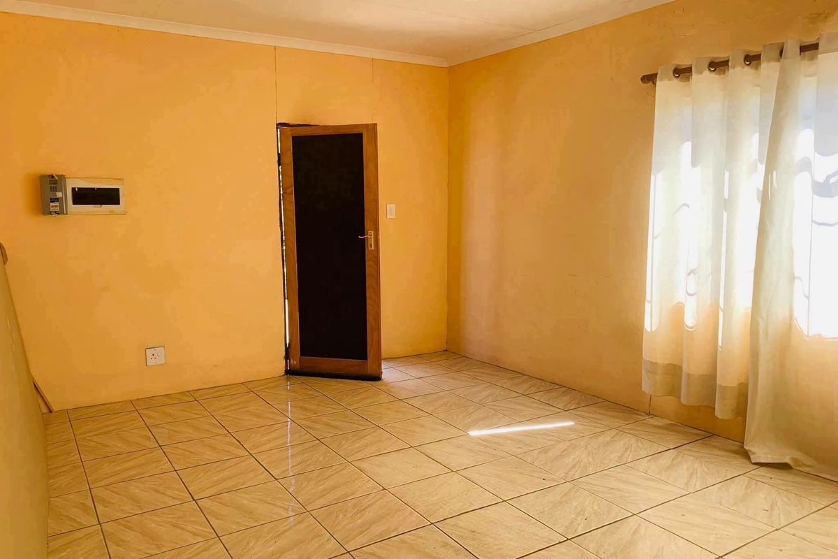 An empty living room featuring tiled flooring, a wall-mounted electrical distribution board, and a curtain rod, ready for personalization.