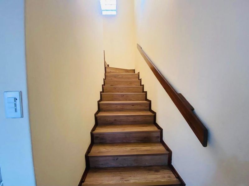 A clean, well-maintained staircase featuring wooden treads and a matching handrail, illuminated by a natural light source from above.