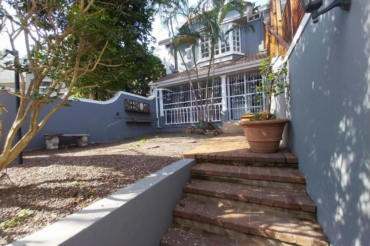 Rear exterior view of the townhouse featuring a brick staircase, gravel garden area, and secure gated entrance to the main dwelling.