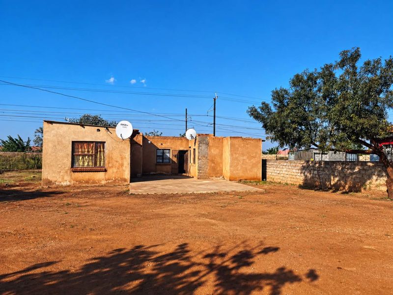 Rear view of the property featuring a concrete patio, stone boundary wall, and a spacious yard area.