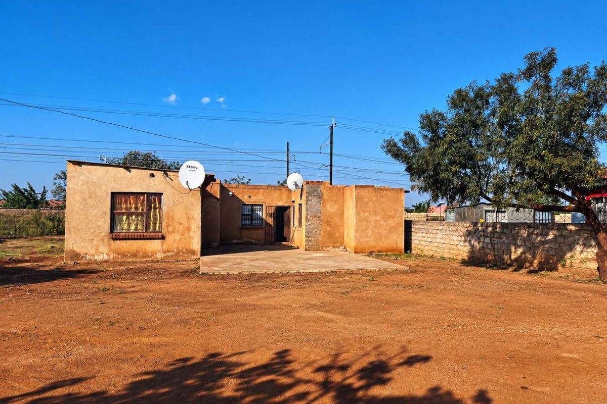 Rear view of the property featuring a concrete patio, stone boundary wall, and a spacious yard area.