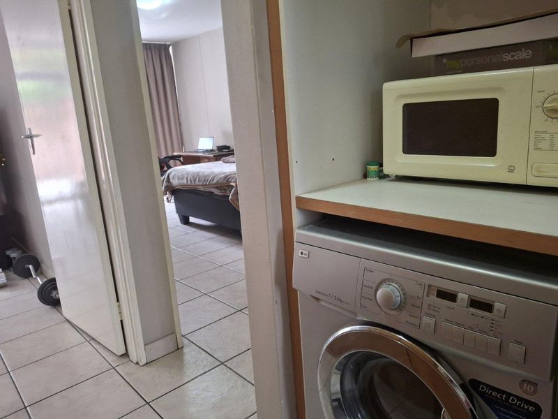 A functional laundry area featuring tiled flooring and built-in cabinetry, with a view through to the adjacent bedroom.