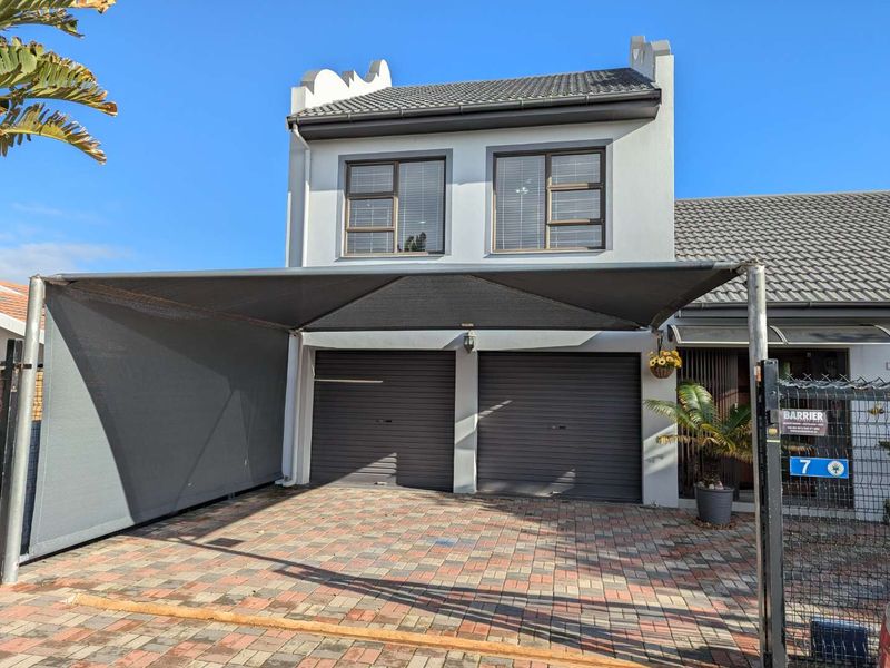 Front elevation of a double-storey house featuring a paved driveway, double garage, and a large shade sail structure.