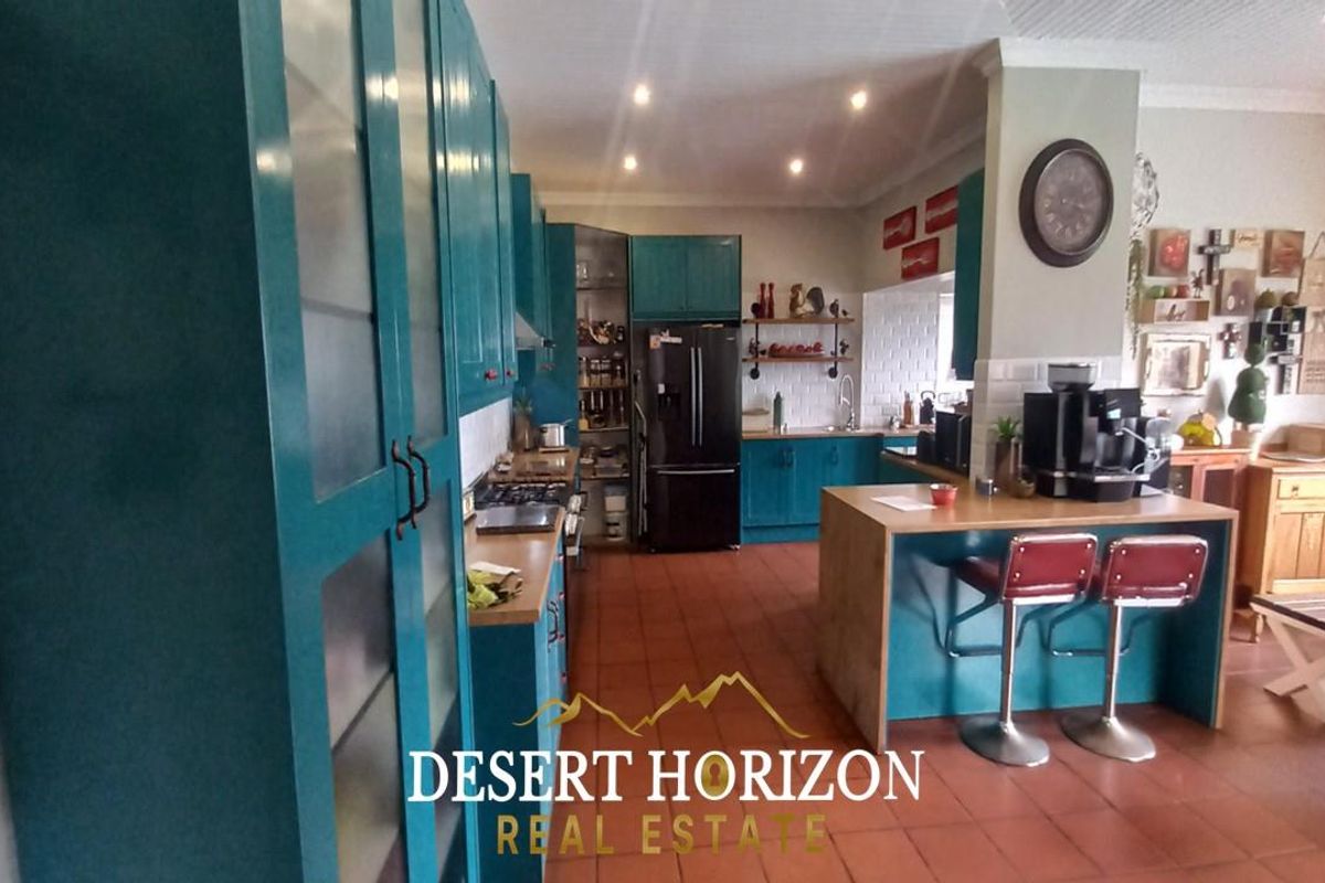 Spacious kitchen featuring teal cabinetry, a central island with breakfast bar seating, tiled flooring, and integrated storage solutions.