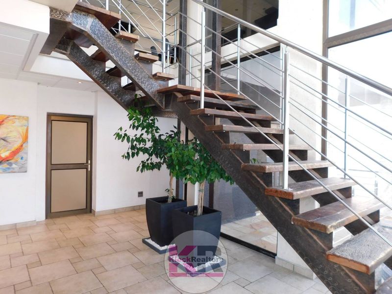 Modern entrance hall featuring a striking open-tread staircase with steel stringers and stainless steel balustrades, complemented by neutral tiled flooring.