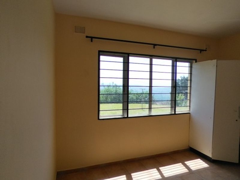 A simple, empty bedroom featuring tiled flooring, a large window with security bars, and neutral wall paint, offering a blank canvas for personalization.